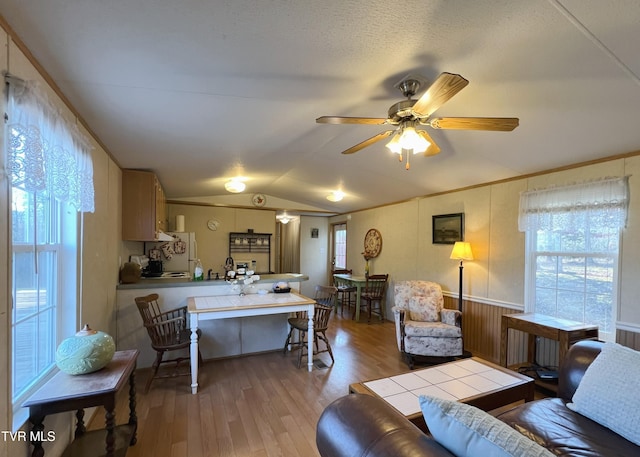 living area with lofted ceiling, wood finished floors, a wealth of natural light, and crown molding