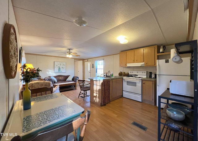 kitchen with white appliances, visible vents, a peninsula, light wood-type flooring, and under cabinet range hood