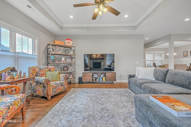 living room featuring ceiling fan, a raised ceiling, light wood-type flooring, and crown molding