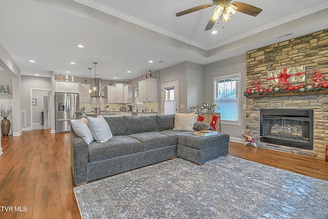 living room featuring ceiling fan, sink, crown molding, wood-type flooring, and a fireplace