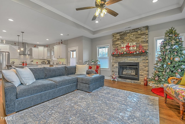 living room with crown molding, ceiling fan, a fireplace, a tray ceiling, and light hardwood / wood-style floors