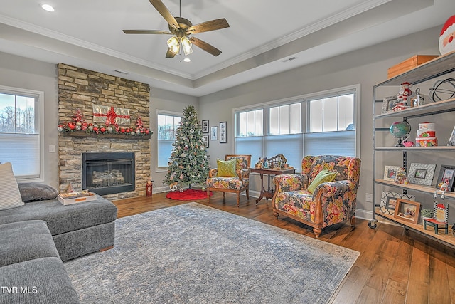 living room featuring ornamental molding, hardwood / wood-style flooring, a stone fireplace, and a healthy amount of sunlight