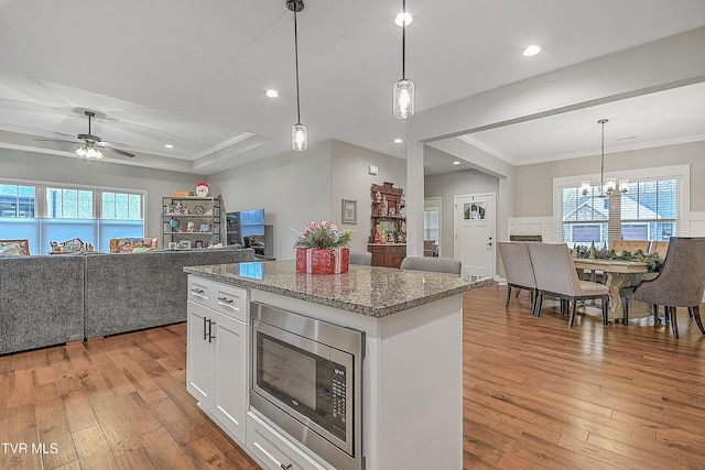 kitchen with stainless steel microwave, white cabinets, ceiling fan with notable chandelier, and light hardwood / wood-style flooring