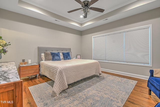 bedroom with hardwood / wood-style floors, ceiling fan, crown molding, and a tray ceiling