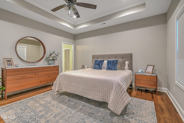 bedroom with ornamental molding, a tray ceiling, ceiling fan, and dark wood-type flooring