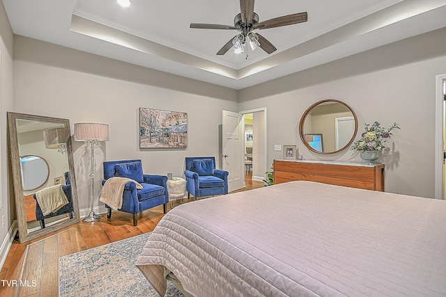 bedroom with hardwood / wood-style floors, ceiling fan, ornamental molding, and a tray ceiling