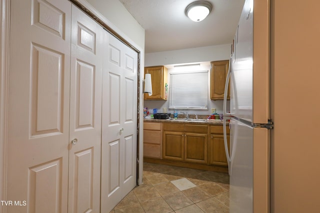 kitchen featuring white refrigerator, light tile patterned floors, and sink