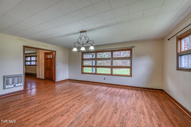 unfurnished room featuring heating unit, a healthy amount of sunlight, a chandelier, and wood-type flooring