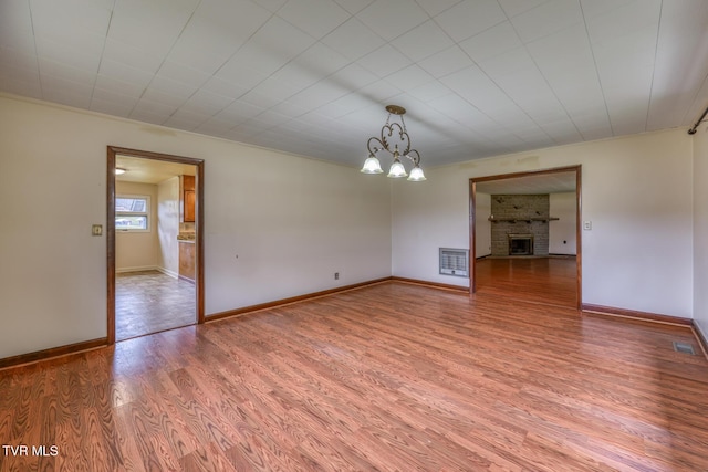 empty room featuring a brick fireplace, hardwood / wood-style flooring, an inviting chandelier, and heating unit