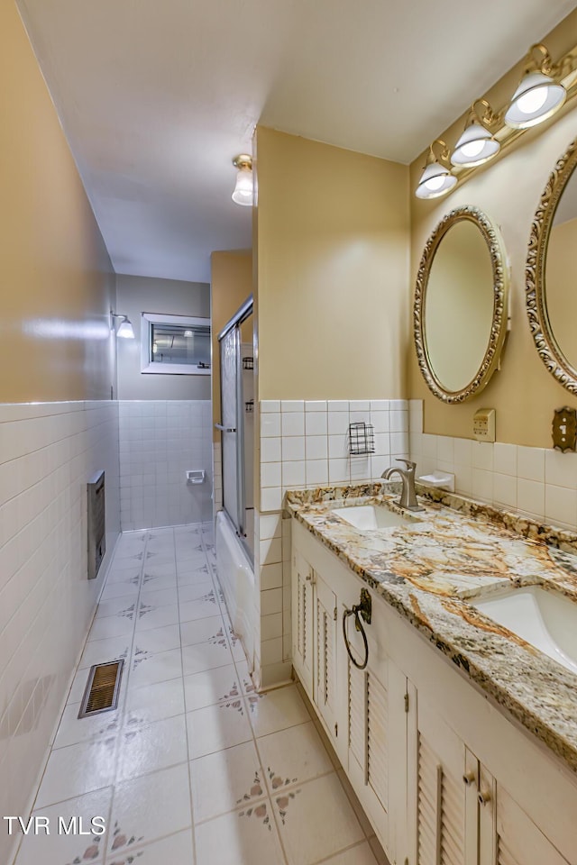 bathroom with tile patterned flooring, vanity, enclosed tub / shower combo, and tile walls