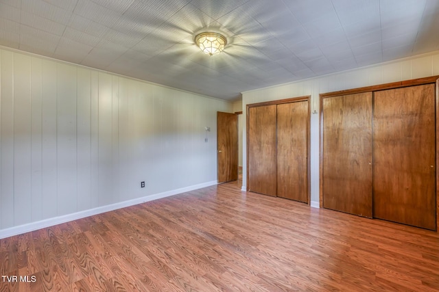 unfurnished bedroom with two closets and light hardwood / wood-style flooring