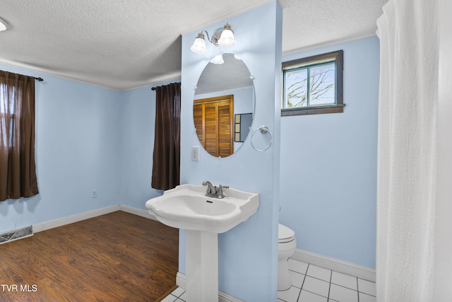 bathroom featuring sink, toilet, wood-type flooring, and a textured ceiling