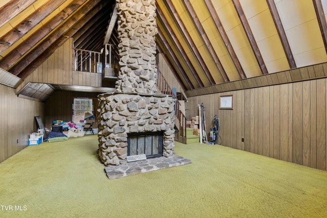 unfurnished living room with carpet flooring, wood walls, a stone fireplace, and high vaulted ceiling