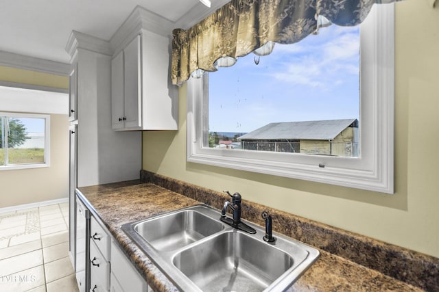 kitchen with white cabinetry, sink, light tile patterned floors, and ornamental molding