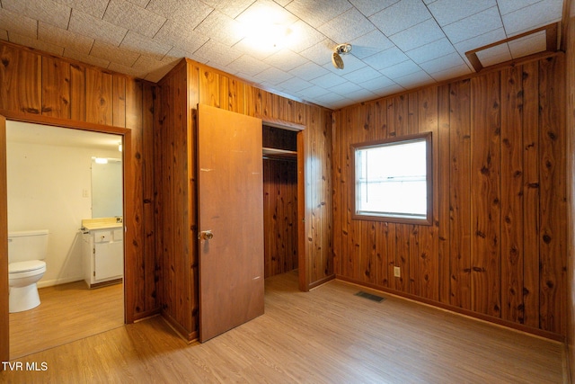 unfurnished bedroom with wood walls, light hardwood / wood-style floors, connected bathroom, and a closet