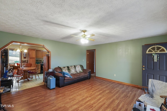 living room with ceiling fan with notable chandelier, light hardwood / wood-style floors, and a textured ceiling