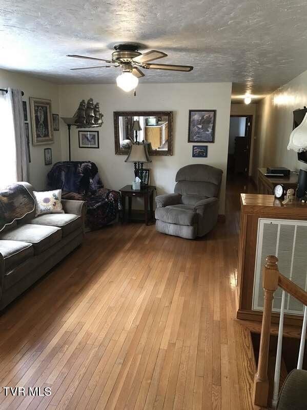 living room with a ceiling fan, visible vents, a textured ceiling, and wood finished floors