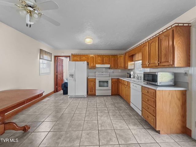 kitchen featuring light tile patterned flooring, under cabinet range hood, white appliances, light countertops, and brown cabinets