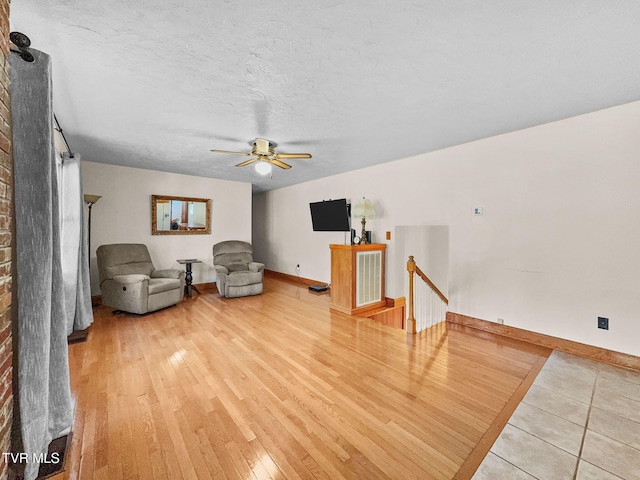 unfurnished room with a textured ceiling, wood finished floors, a ceiling fan, an upstairs landing, and baseboards