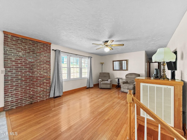 living area with a textured ceiling, ceiling fan, brick wall, wood finished floors, and baseboards