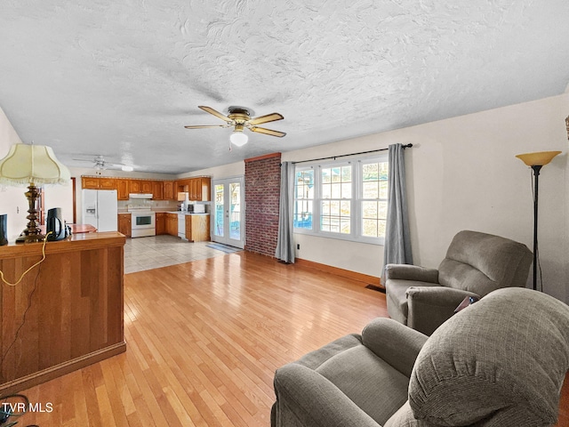 living area with light wood-style flooring, baseboards, ceiling fan, and a textured ceiling