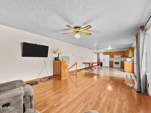 living area with baseboards, ceiling fan, a textured ceiling, and light wood finished floors