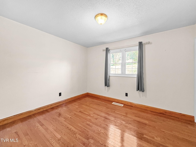 empty room featuring baseboards, a textured ceiling, visible vents, and wood finished floors