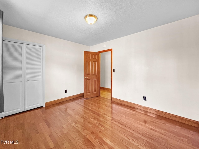 unfurnished bedroom featuring light wood-style floors, a closet, a textured ceiling, and baseboards