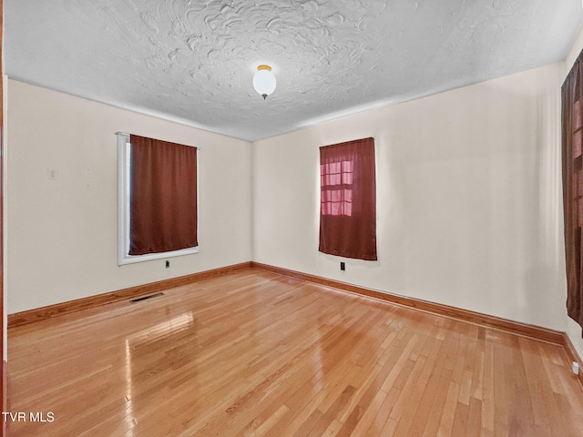 empty room with baseboards, a textured ceiling, visible vents, and wood finished floors