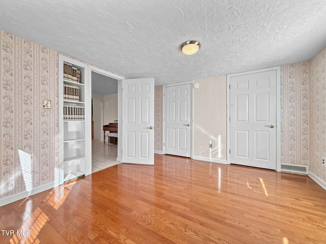 unfurnished bedroom featuring a textured ceiling, wood finished floors, visible vents, and wallpapered walls