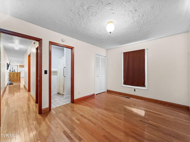 unfurnished bedroom featuring a textured ceiling, baseboards, and light wood-style floors