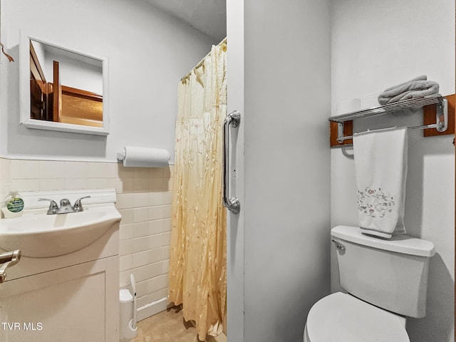 bathroom with tile walls, a wainscoted wall, vanity, and toilet