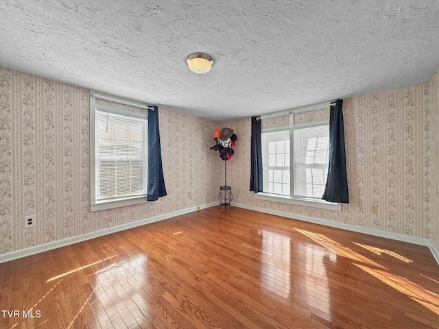 spare room with wood finished floors, baseboards, and wallpapered walls