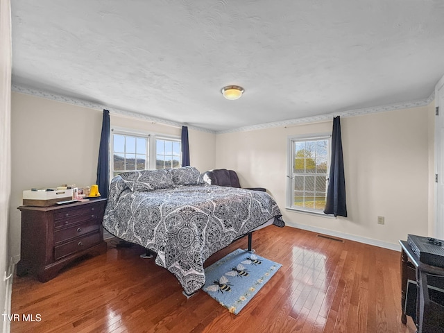 bedroom with baseboards, multiple windows, visible vents, and wood finished floors