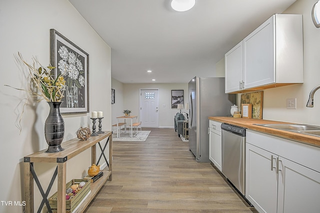 kitchen with dishwasher, wooden counters, sink, light wood-type flooring, and white cabinetry