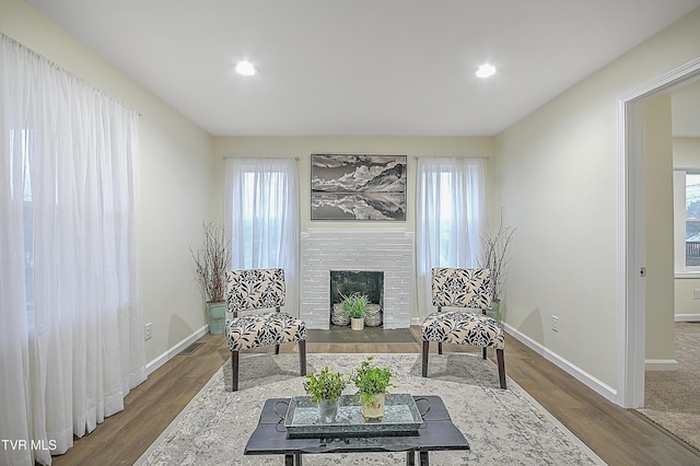 sitting room with a brick fireplace, plenty of natural light, and hardwood / wood-style flooring