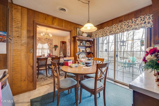 dining room with a chandelier, a wealth of natural light, and wooden walls