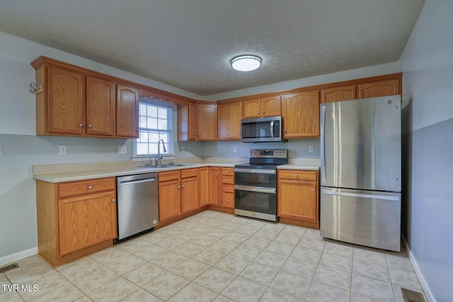 kitchen featuring sink, light tile patterned flooring, stainless steel appliances, and a textured ceiling