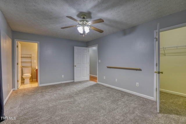 unfurnished bedroom with a textured ceiling, a walk in closet, light colored carpet, and ceiling fan