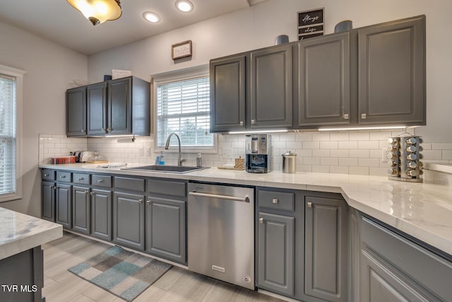 kitchen with gray cabinetry, sink, stainless steel dishwasher, light stone countertops, and tasteful backsplash