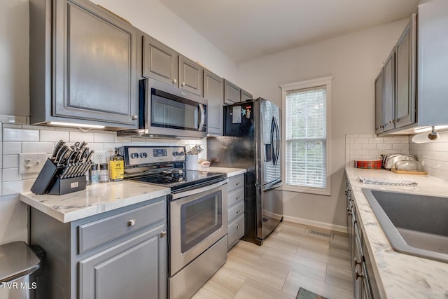 kitchen featuring decorative backsplash, appliances with stainless steel finishes, light stone counters, and sink