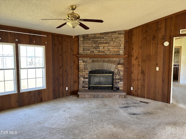 unfurnished living room featuring a textured ceiling, a stone fireplace, ceiling fan, and wood walls