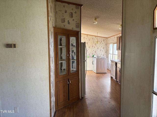 hallway with hardwood / wood-style flooring, a notable chandelier, crown molding, and washing machine and clothes dryer