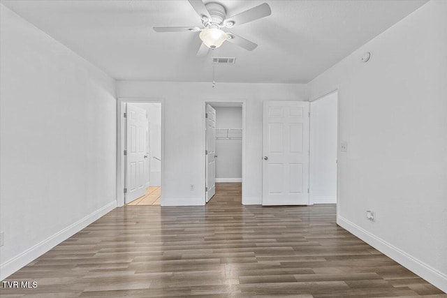 unfurnished bedroom featuring dark hardwood / wood-style flooring, a closet, a spacious closet, and ceiling fan