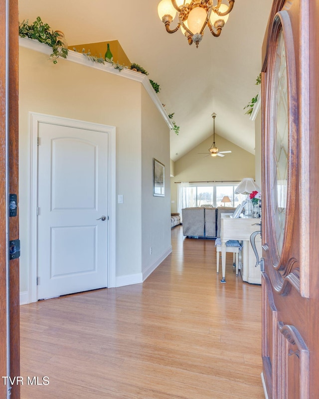 foyer featuring vaulted ceiling, ceiling fan with notable chandelier, light wood-type flooring, and baseboards