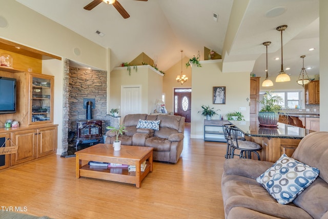 living room with visible vents, a wood stove, light wood-style floors, high vaulted ceiling, and ceiling fan with notable chandelier