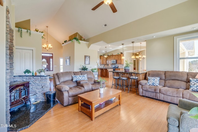 living area featuring a wood stove, light wood-style floors, visible vents, and ceiling fan with notable chandelier