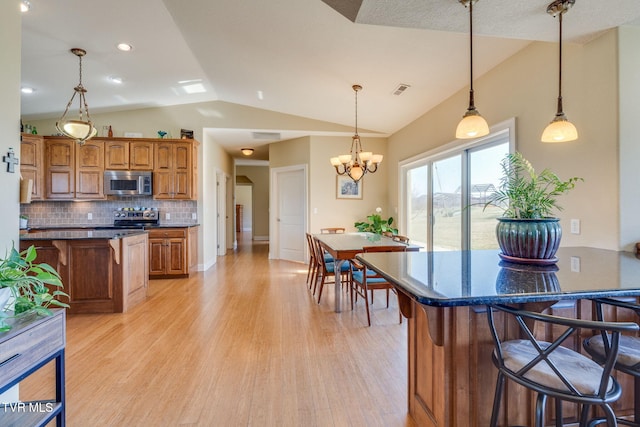 kitchen featuring a breakfast bar area, stainless steel appliances, vaulted ceiling, brown cabinets, and dark countertops