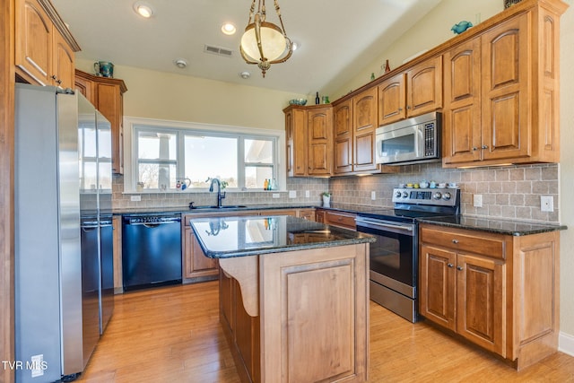 kitchen with stainless steel appliances, dark stone counters, a sink, and backsplash