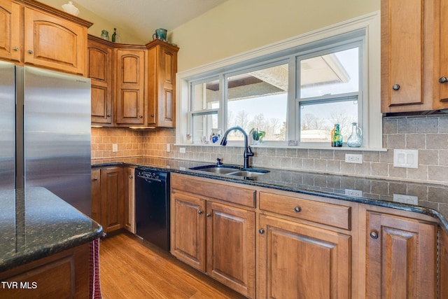 kitchen with black dishwasher, tasteful backsplash, brown cabinetry, a sink, and stainless steel fridge